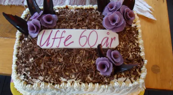 En tårtbotten i långpanna dekorerad med chokladspån, lila rosor och texten "Uffe 60 år".