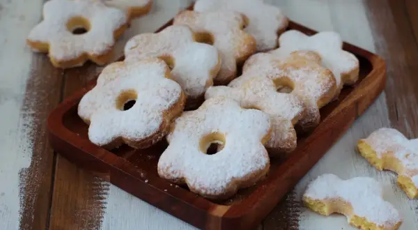 Deliziosi dolci solo tuorli benedetta, a forma di fiore, cosparsi di zucchero a velo su un vassoio di legno.