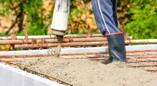 Betoniarz w gumowcach kieruje strumień betonu z pompy na zbrojenie. Waga betonu jest kluczowa dla wytrzymałości konstrukcji.