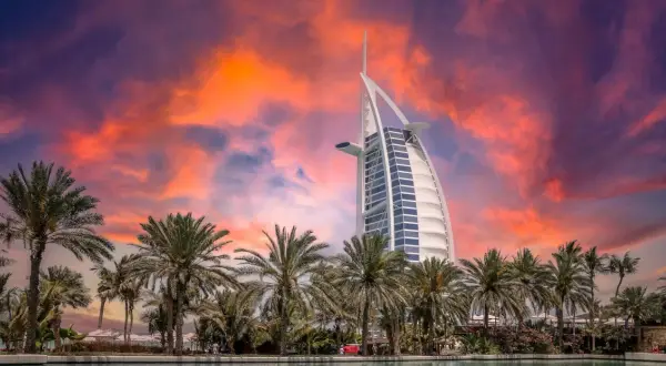 Zachód słońca nad Dubajem z palmami i hotelem Burdż al-Arab. Zastanawiasz się, ile kosztuje wycieczka do Dubaju?