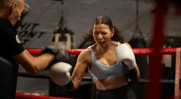 Intense boxing warm up: a woman throws a punch with fierce determination as her trainer holds pads.