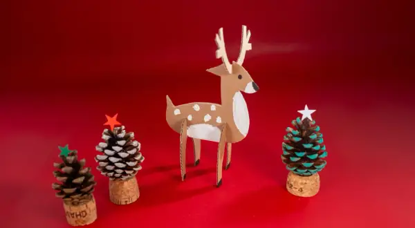 Julpynt med kottar: en papphjort och tre små julgranar gjorda av kottar, korkar och stjärnor.