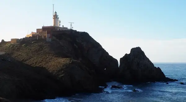 Faro en la cima de un acantilado rocoso sobre la cala del corralete. El mar azul choca contra las rocas.