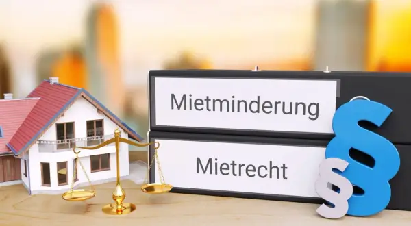 Hausmodelle, Waage der Gerechtigkeit und Ordner mit "Mietminderung" und "Mietrecht" – ein Symbol für die Bewertung von Wasserschäden.