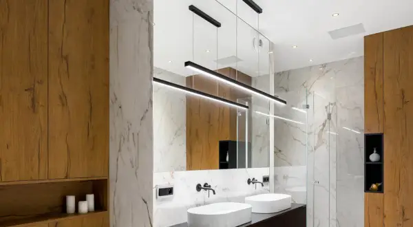 Bagno moderno con lavabi bianchi, specchio ampio e moderne idee illuminazione bagno con lampade a sospensione nere.