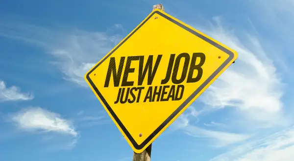 Gul varningsskylt med texten "NEW JOB JUST AHEAD" mot en blå himmel med moln. Perfekt för den som trivs inte på jobbet och söker nya utmaningar.
