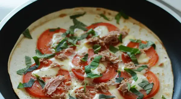 Pyszna pizza z tortilli z tuńczykiem, pomidorami i bazylią, przygotowywana na patelni.