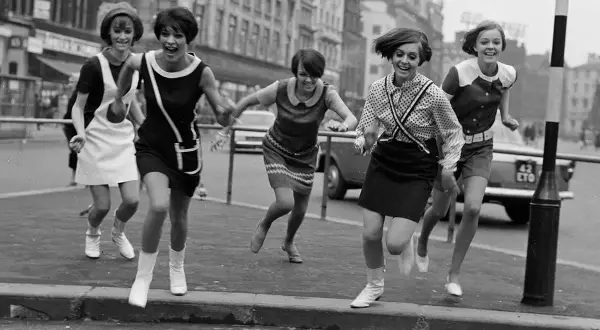 Cinco chicas con minivestidos y botas, al estilo de Mary Quant, corren alegres por la calle.