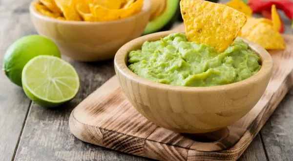 Miseczka z guacamole, nachos, limonki i awokado na drewnianym stole.