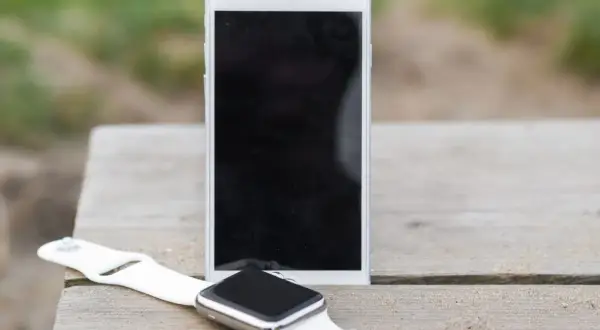Biały smartwatch i smartfon leżą na drewnianym stole. Dowiedz się, jak sparować zegarek z telefonem, by cieszyć się nowymi możliwościami.