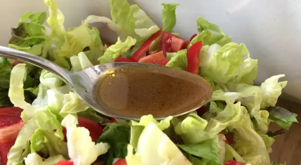 Löffel mit balsamico dressing über frischem Salat mit Tomaten und Paprika.