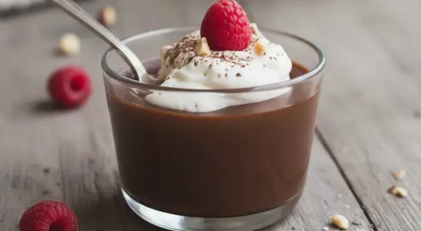 Delizioso budino fatto in casa al cioccolato, guarnito con panna montata, un lampone fresco e nocciole croccanti.