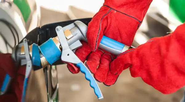 Ręce w czerwonych rękawicach podłączają pistolet do tankowania LPG. Sprawdzanie aktualnej lpg cena to klucz do oszczędności.