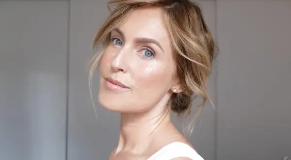 En kvinna med blå ögon och blont hår visar hur man får glow i ansiktet med naturlig makeup och lyster.