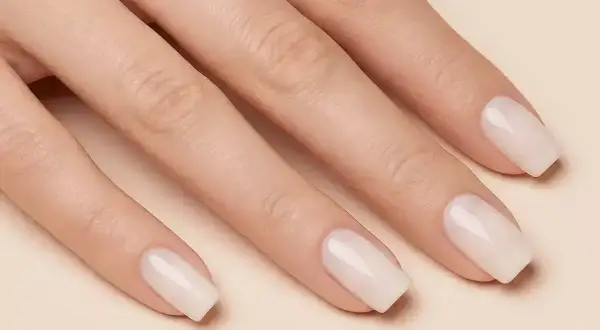 Dłoń z idealnie zadbanymi, klasycznymi paznokciami w mlecznym kolorze. Delikatny manicure podkreśla naturalne piękno.