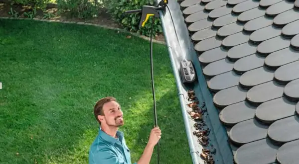 Hombre sonriente usando un accesorio para limpiar canalones altos con una hidrolimpiadora.