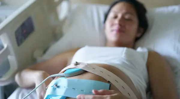 Une femme enceinte est allongée, un moniteur de rythme cardiaque fœtal est fixé sur son ventre. Ce monitoring sert à surveiller le bien-être du bébé.