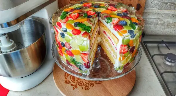 Kolorowy tort z galaretką i owocami, gdzie dekoracyjne układanie owoców tworzy tęczową mozaikę.