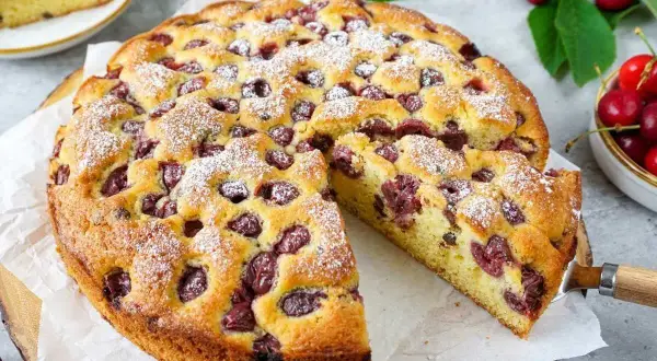 Saftiger kirschkuchen mit frischen kirschen, bestäubt mit Puderzucker. Ein Stück wurde bereits herausgeschnitten.