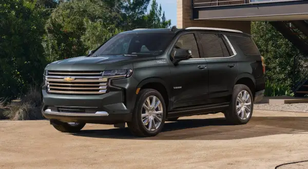 Ciemnozielony Chevrolet Tahoe High Country z chromowanymi felgami stoi przed nowoczesnym domem.