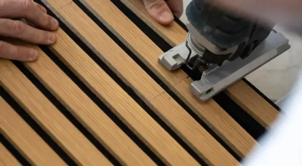 Mani che guidano un seghetto alternativo per tagliare pannelli fonoassorbenti in legno.