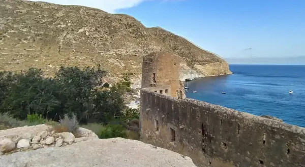 Ruinas de un castillo en cala san pedro, con el mar azul y montañas al fondo.