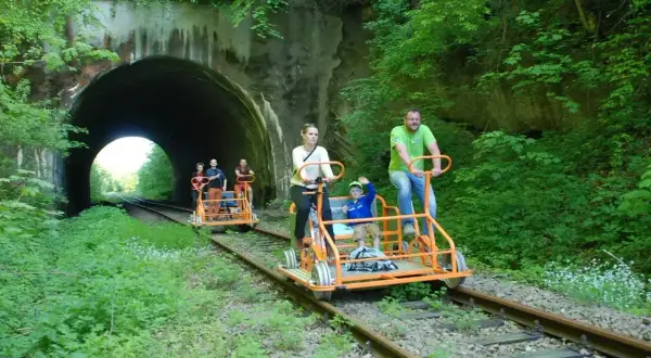 Rodzina na drezynach w Bieszczadach pokonuje malowniczy tunel kolejowy, ciesząc się zielenią i aktywnym wypoczynkiem.