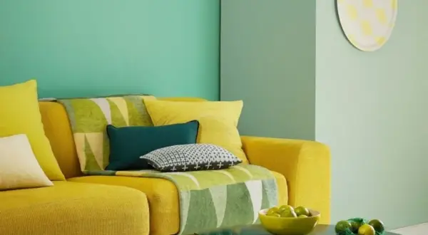 Divano giallo acceso con cuscini colorati e una coperta con motivi geometrici in **colore verde**. Sul tavolino, una ciotola di lime.