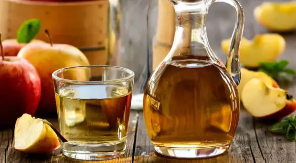 Aceto di mele in caraffa e bicchiere, con mele fresche. Un rimedio naturale per un bucato morbido.