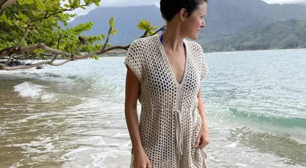 Donna in costume uncinetto beige, con sfondo mare e montagne. Perfetto schema costume uncinetto per l'estate.