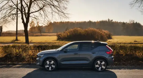 Szary Volvo EX40 zaparkowany na poboczu drogi, w tle jesienny krajobraz z drzewami i krzewami.