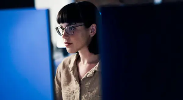 Junge Frau mit Brille und Kurzhaarschnitt, konzentriert auf einen Bildschirm. Sie repräsentiert eine der vielen Berufe mit Zukunft in der digitalen Welt.