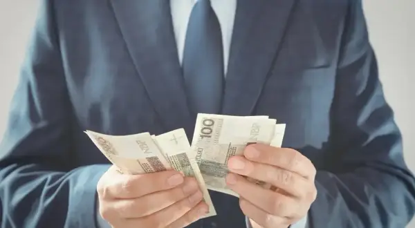 Mężczyzna w garniturze liczy banknoty 100 zł. Czy to jego zarobki jako członka rady osiedla?