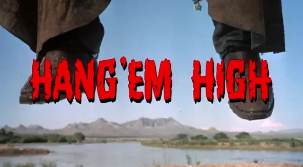 Nogi w kowbojkach wiszą nad rzeką. Czerwony napis "HANG 'EM HIGH" sugeruje westernowe porachunki.