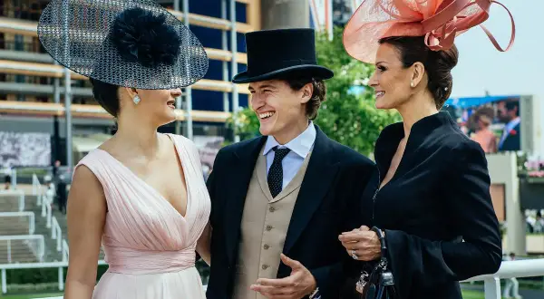Elegancki francuski arystokrata w cylindrze i dwie damy w ozdobnych kapeluszach, uśmiechają się do siebie na wyścigach.