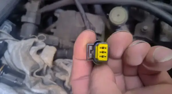 Wtyczka z żółtym wkładem, być może związana z błędem **dtc p1693 volkswagen**. W tle widać fragmenty silnika.