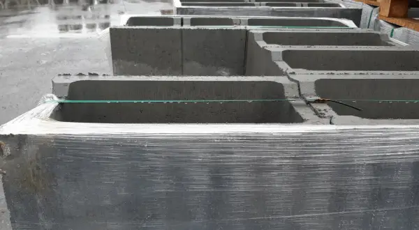 Stos betonowych bloczków zalewowych, owiniętych folią, czeka na budowę.