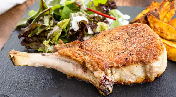 Saftiges Kotelett im Backofen, goldbraun gebraten, serviert mit knusprigen Kartoffelspalten und frischem Salat.