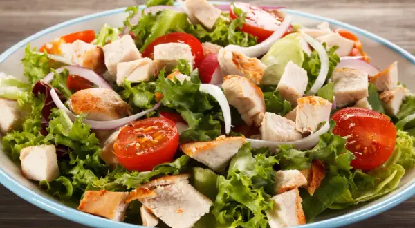Insalata di pollo fresca con lattuga croccante, pomodorini succosi, cipolla rossa e pezzi di pollo grigliato.
