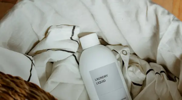 Una botella de líquido para la colada descansa entre la ropa blanca, lista para que el lino se dé de sí.