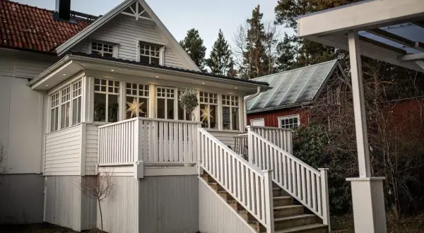 Vitt hus med glasveranda, stjärnor i fönstren och en röd stuga i bakgrunden. Glasveranda inspiration för ett mysigt hem.