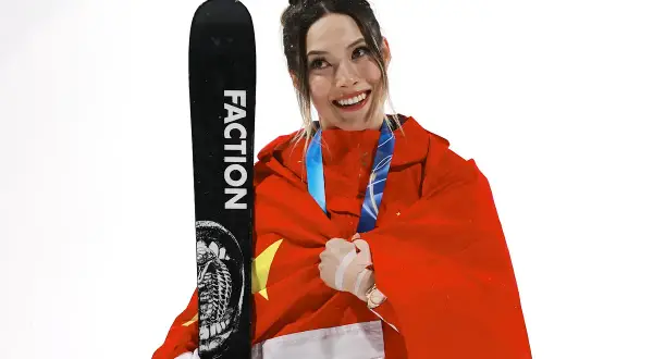 Eileen Gu, sonriente y envuelta en la bandera china, sostiene un esquí Faction.