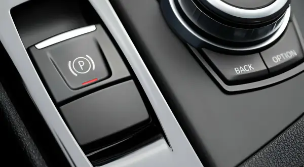 Bouton de frein à main électronique avec voyant rouge allumé, prêt à lâcher assurance. Le bouton "P" est visible.