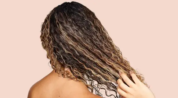Cabello rizado y húmedo con reflejos dorados, mostrando cómo fortalecer el pelo con productos nutritivos.