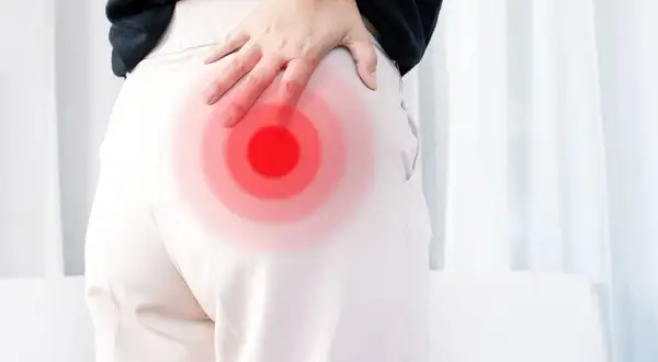 Person håller handen mot höften där en röd cirkel indikerar smärta, möjligen relaterad till piriformis triggerpunkt.