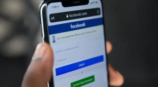 Dłoń trzyma smartfon z ekranem logowania Facebooka. Szukasz sposobu, jak odzyskać konto na FB bez maila i telefonu?