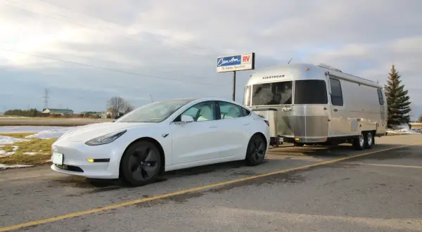Une voiture électrique blanche tracte une caravane Airstream argentée. La question "peut on tracter avec une voiture electrique" trouve ici une réponse visuelle.