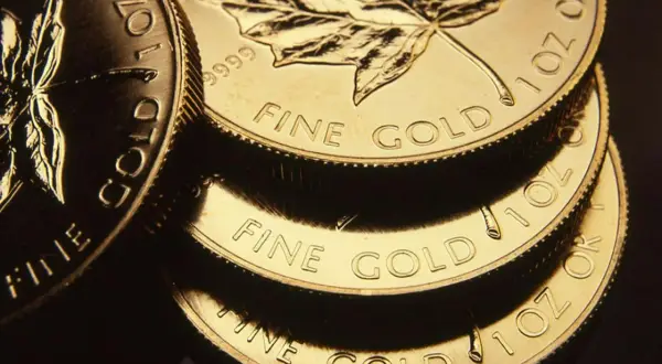 Stos złotych monet z liściem klonu i napisem "FINE GOLD".