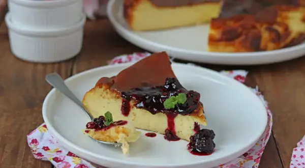 Una fetta di cheesecake basca cremosa, con topping di frutti di bosco e menta, su un piatto bianco.