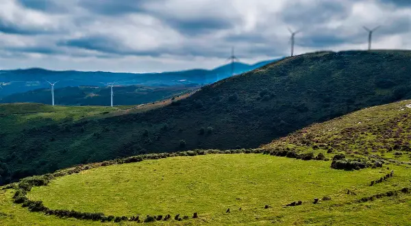 Prado das Chantas, un paisaje verde con molinos de viento en colinas onduladas bajo un cielo nublado.